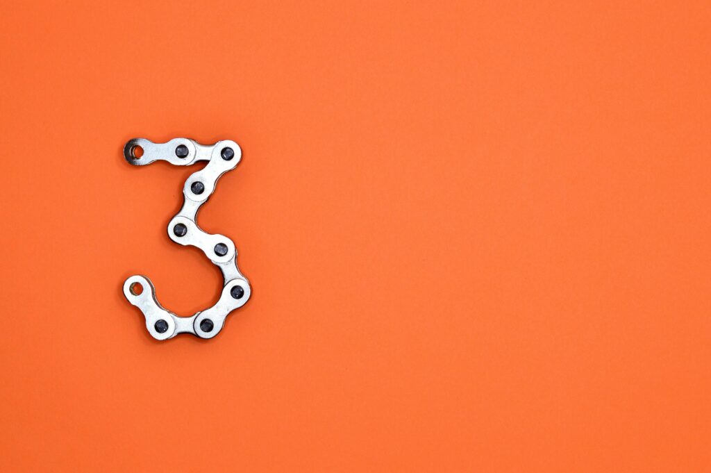 Number 3 shaped from a bicycle chain on an orange background, symbolizing 3 powerful debt-crushing hacks for faster financial freedom.