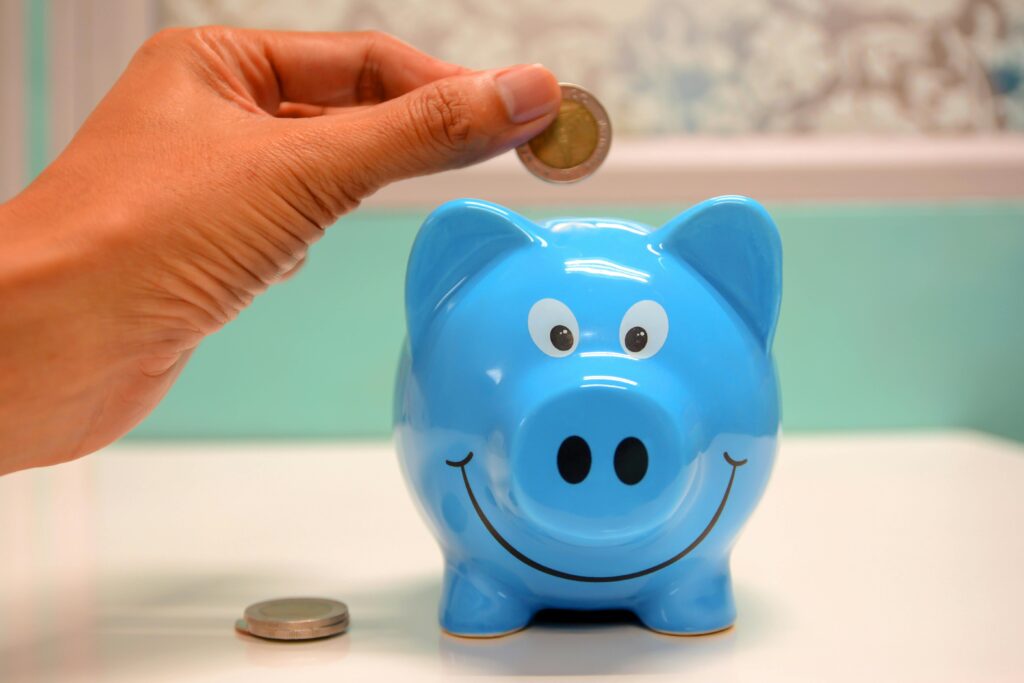 Saving hacks: Hand placing a coin into a blue piggy bank for smart money management.